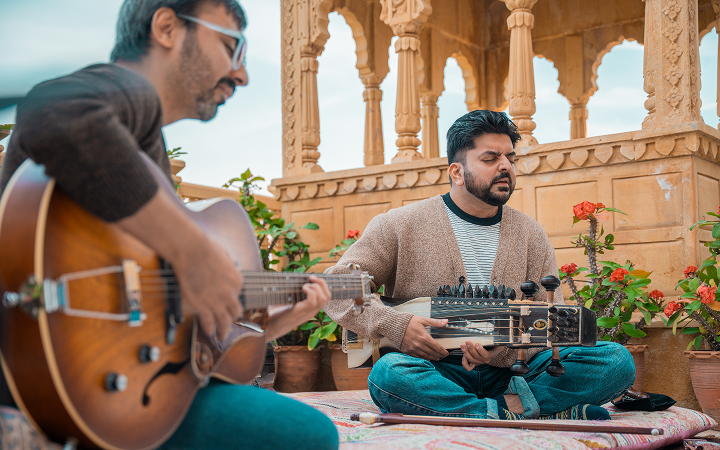 Two musicians playing on a rooftop courtyard with stone architecture behind