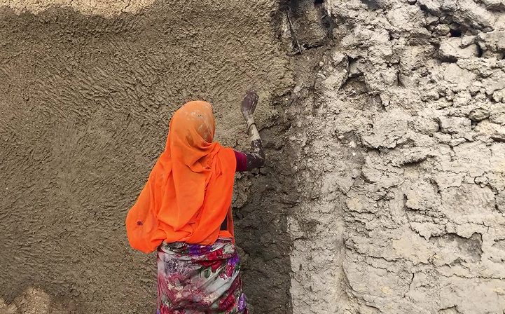 A woman at Dhun finishing a mud-plastered wall by hand